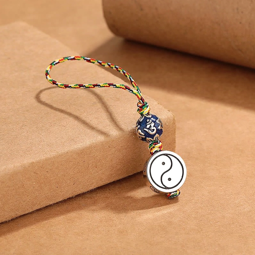 Flat lay view of Yin Yang protective keychain with silver-toned Bagua pendant, colorful woven rope, and blue mantra bead