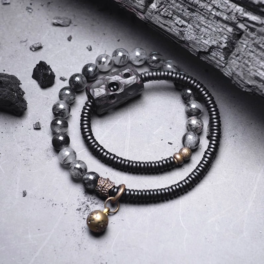 Two-strand black rutilated quartz and ebony wood bracelet with carved wood accent and brass hardware on gray tabletop