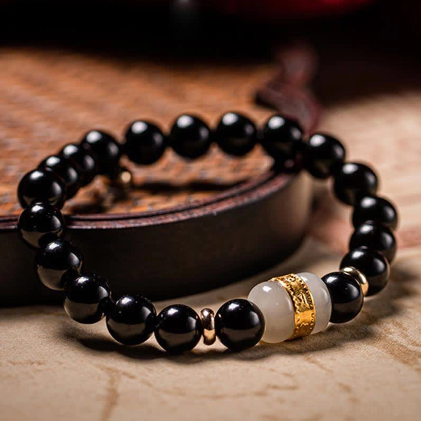 Matching pair of black obsidian and jade couples bracelets coiled together on wooden tray with leather accent, featuring decorative gold spacer details