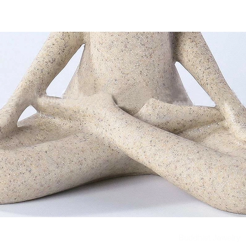 Low close-up front view of cross-legged yoga meditation figurine showing detailed limbs and speckled beige resin texture