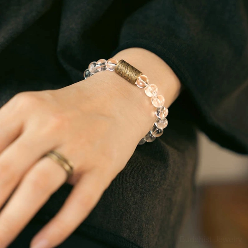 Buddhist crystal bracelet on inner wrist paired with gold ring on dark fabric background