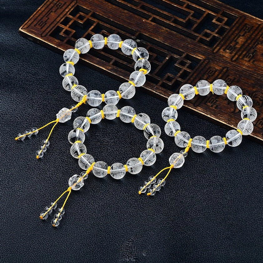 Multiple white crystal Buddhist prayer bracelets with engraved Heart Sutra beads, yellow spacer beads, and crystal tassel pendants on carved wooden background
