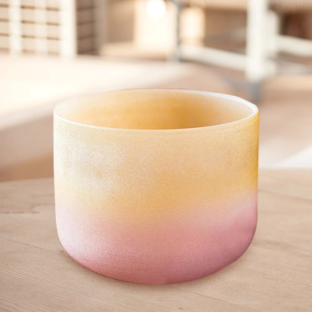 Handmade crystal healing singing bowl with warm yellow-pink gradient on light wooden table, showing smooth frosted surface finish and acoustic design