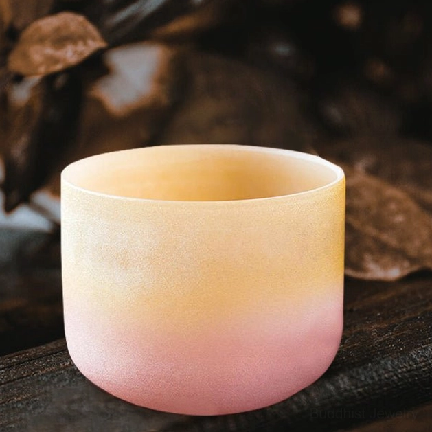 Buddhist crystal singing bowl displayed on dark wood surface with dry botanicals, showcasing matte frosted texture and natural yellow-pink color gradient