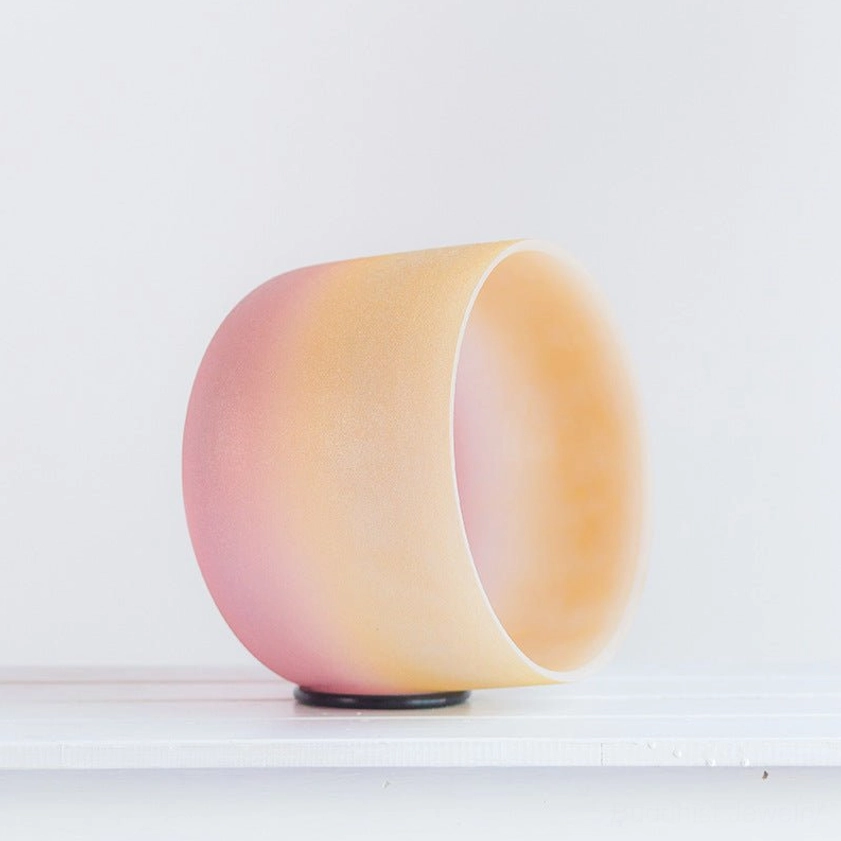 Side profile of handcrafted crystal singing bowl with yellow-pink matte texture and black base pad, minimalist white background, showing complete bowl dimensions