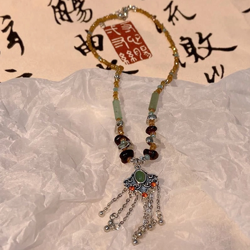 Spiritual crystal tassel pendant necklace close-up showing gold-toned and mixed gemstone beads with silver dangling tassel charm on calligraphy inspired backdrop