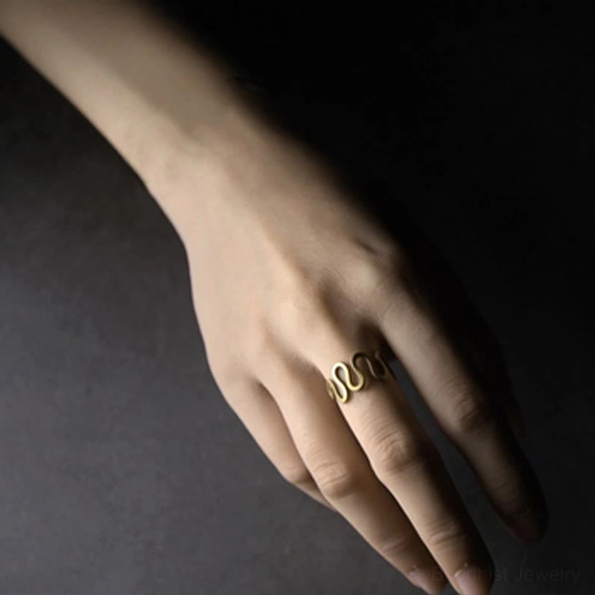 Hand wearing curved brass wave ring side close-up view showing antique brass finish and elegant wavy pattern