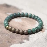 Cyan bodhi seed copper bracelet flat lay featuring barrel-shaped cyan beads with vintage bronze textured spacer beads on sand and wood background