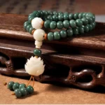 Cyan bodhi seed lotus bracelet overhead view on wooden table, showing natural matte green beads with white lotus charm and decorative tassel - Buddhist prayer beads for meditation