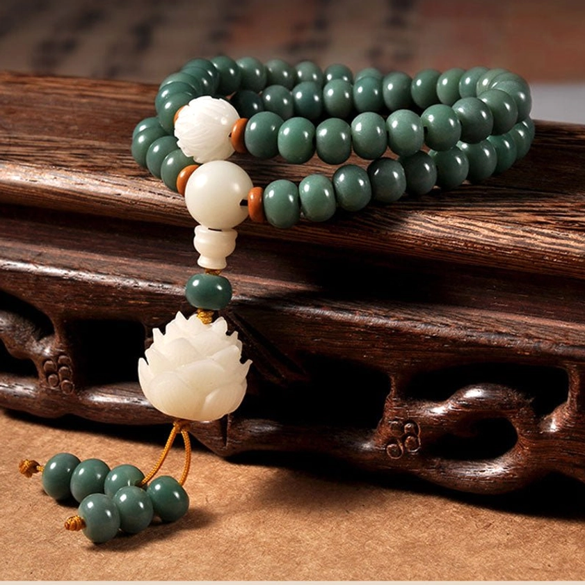 Cyan bodhi seed lotus bracelet overhead view on wooden table, showing natural matte green beads with white lotus charm and decorative tassel - Buddhist prayer beads for meditation