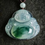 Handcrafted cyan jade laughing Buddha pendant with carved smiling Buddha face and dark green jade veining, displayed on dark stone background with brown waxed cord
