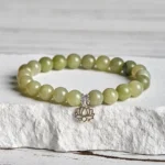 Cyan jade lotus bracelet with 925 sterling silver charm displayed on white stone, showing gradient green beads and hollow lotus pendant
