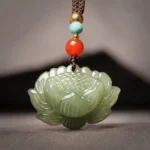Hetian cyan jade lotus flower pendant necklace with multi-color beaded rope, flat lay front view on dark background showing carved 3D lotus design