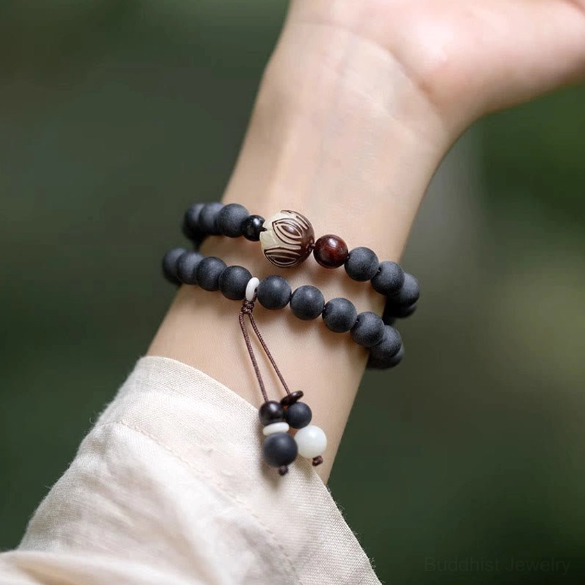 Stacked cypress bodhi prayer bracelet with carved lotus bead and tassel accent worn on wrist outdoors