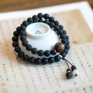 Double-layer cypress bodhi lotus prayer bracelet flat lay on aged calligraphy paper with hand-carved bodhi bead and decorative tassel