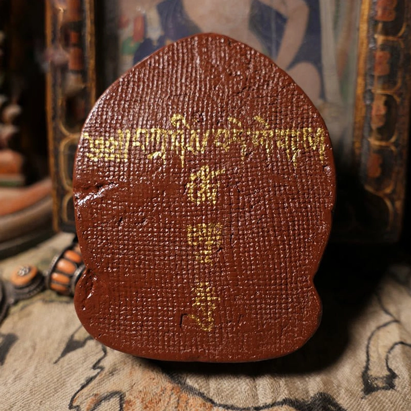 Back view of hand-painted Daikokuten Buddha tsa tsa clay statue with traditional Tibetan script inscriptions and brown clay texture
