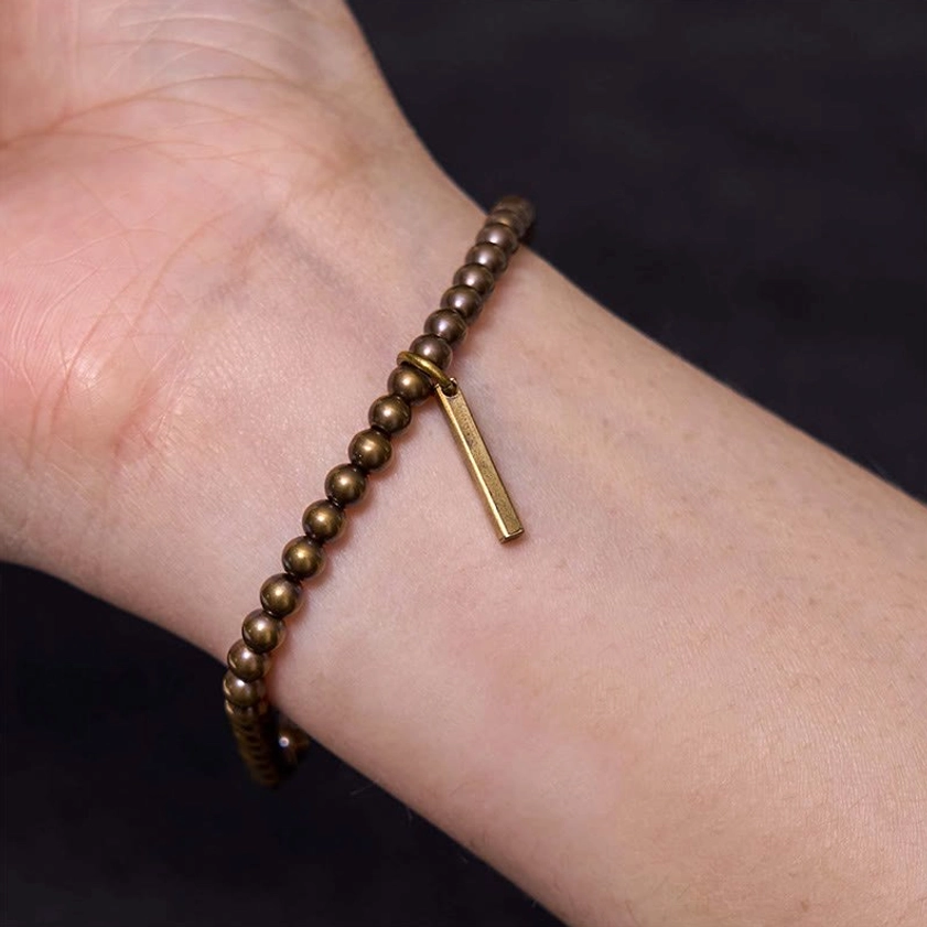 Blackened bronze copper beaded bracelet close-up on wrist showing tight slim fit against grey top background