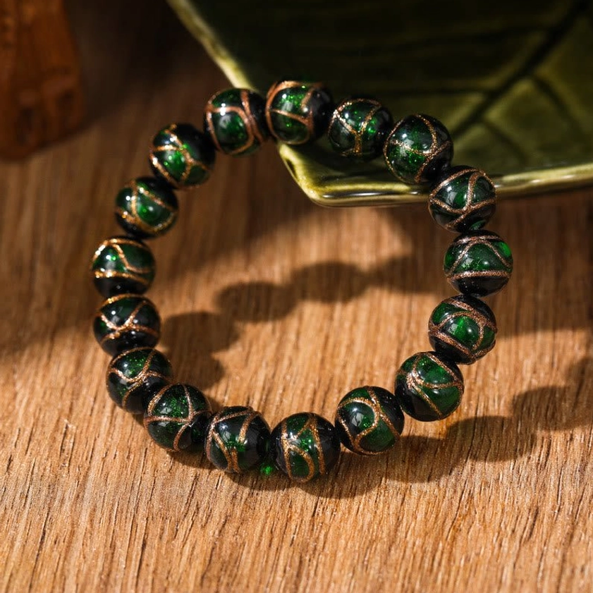 Dark green glossy liuli glass Buddhist bracelet with golden line details viewed flat on wooden surface with natural decor