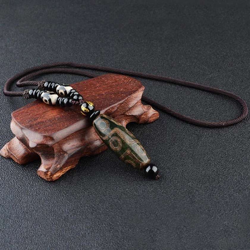 Dark green nine-eye dzi bead necklace with intricate eye pattern on braided cord and decorative bead accents