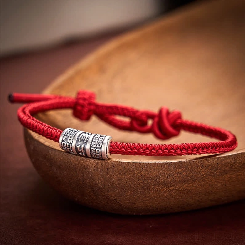 Dark red handmade Buddhist string bracelet with silver Om Mani Padme Hum bead and wooden bowl backdrop