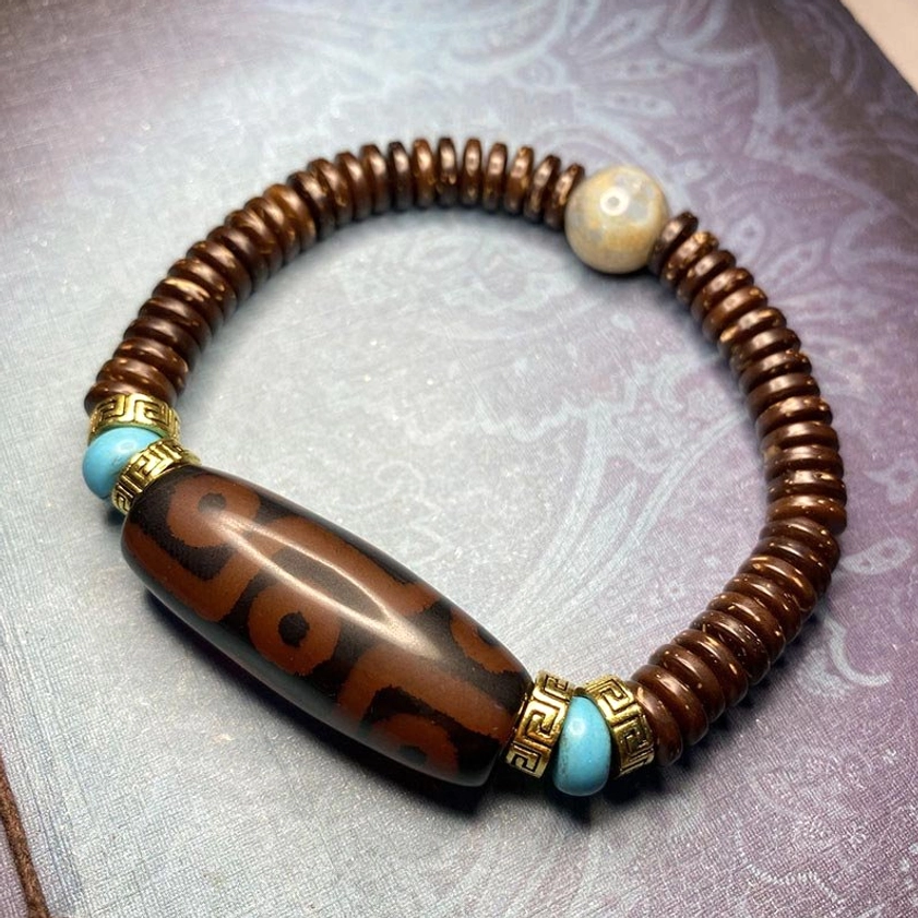 dark red nine-eye dzi bead bracelet with polished surface, turquoise spacers, and gold-toned hardware in authentic Buddhist style