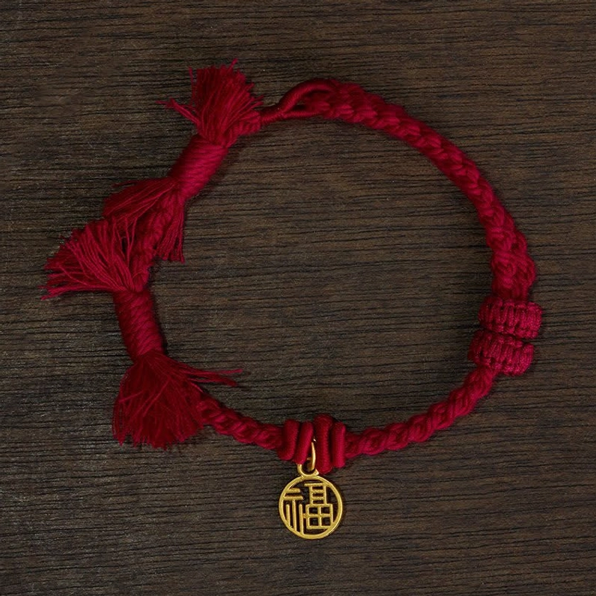 Dark red fu character bracelet flat lay showing burgundy cord with gold round fu charm and tasseled ends