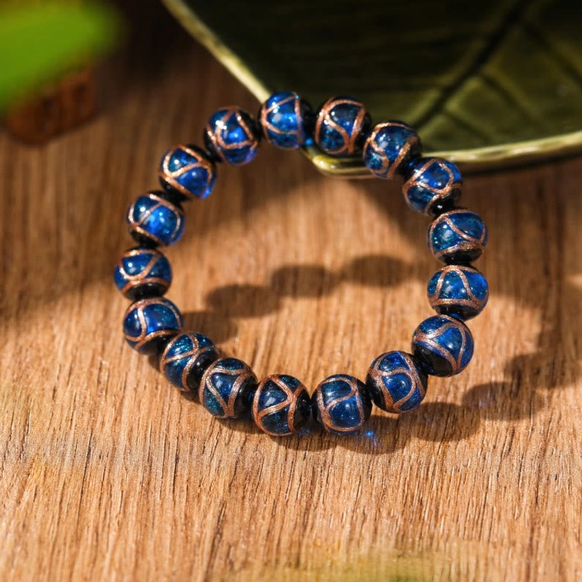 Deep blue glossy liuli glass Buddhist bracelet with golden stripe accents on wooden table with green leaf background