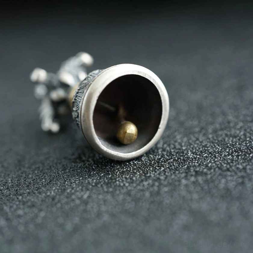 Side lying view of sterling silver dorje bell pendant revealing brass clapper mechanism inside the bell cavity