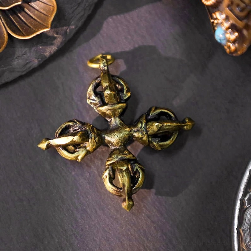 Double cross dorje pendant with intricate four-pointed ritual carving in brassy gold finish, top-down close-up view on dark fabric
