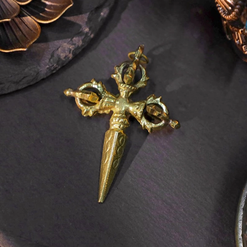 Pointed double dorje pendant with intricate carved Buddhist ritual shape displayed on slate stone surface, close-up angled view