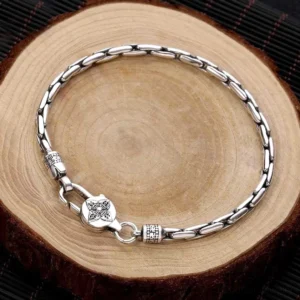 Double Dorje Om Mani Padme Hum Buddhist silver bracelet flat lay top view with linked curb chain and carved metal clasp on wooden background