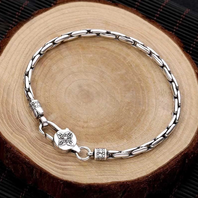 Double Dorje Om Mani Padme Hum Buddhist silver bracelet flat lay top view with linked curb chain and carved metal clasp on wooden background