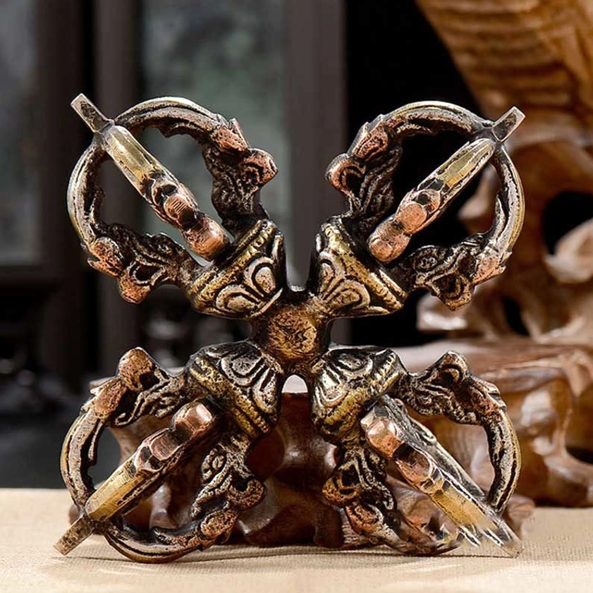 Front eye-level closeup of double dorje vajra on wooden display stand showing intricate carved ritual details and copper tones