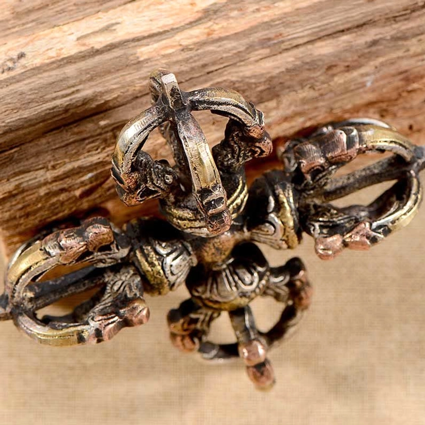 Three-quarter overhead view of symmetrical double dorje vajra on weathered wooden log - Buddhist thunderbolt symbol