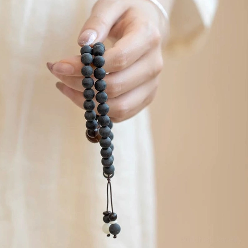 Hand-held double-layer cypress prayer bracelet with long hanging tassel and layered bead charms on linen fabric