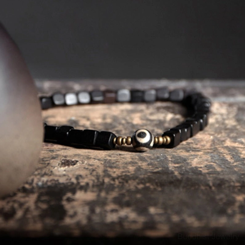 Double-layered ebony bracelet with hand-painted dzi bead and bronze spacers on rustic wood