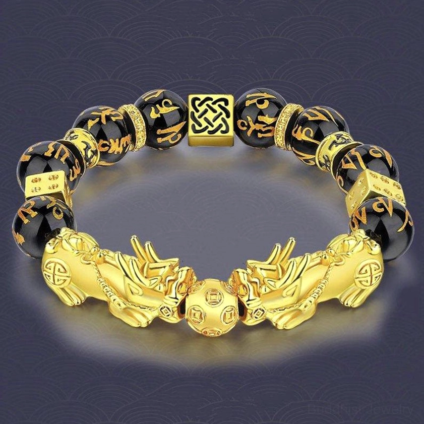 Buddhist Pixiu prosperity bracelet overhead view showing symmetric gold Pixiu charms, central round mantra bead, and Celtic knot spacer on textured grey background