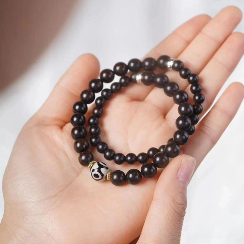 Double wrap dzi bead wooden bracelet with dark ebony wood beads patterned dzi charm displayed in open palms overhead view