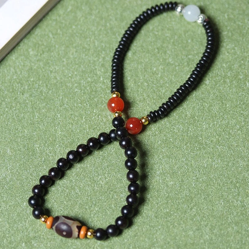 Figure-eight layout flat lay of sacred Buddhist protection bracelet with double strands and central dzi bead accent on green fabric
