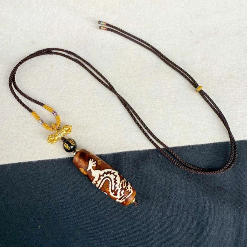 Top view of handcrafted dragon pattern dzi bead Buddhist necklace showing adjustable braided cord and stone pendant detail