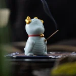 Dragon bell ceramic incense burner in vibrant blue glaze with golden horns and red bell collar, rear three-quarter view on tea mat
