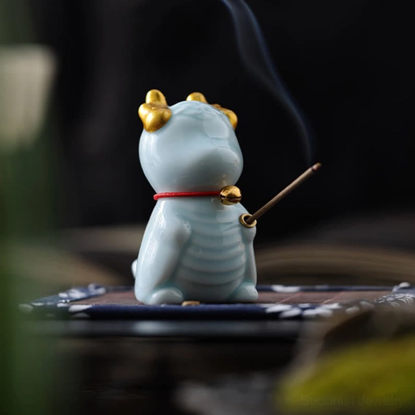 Dragon bell ceramic incense burner in vibrant blue glaze with golden horns and red bell collar, rear three-quarter view on tea mat