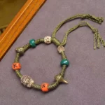 Handmade green rope Buddhist dragon bracelet with carved bead and adjustable tassel on wooden background