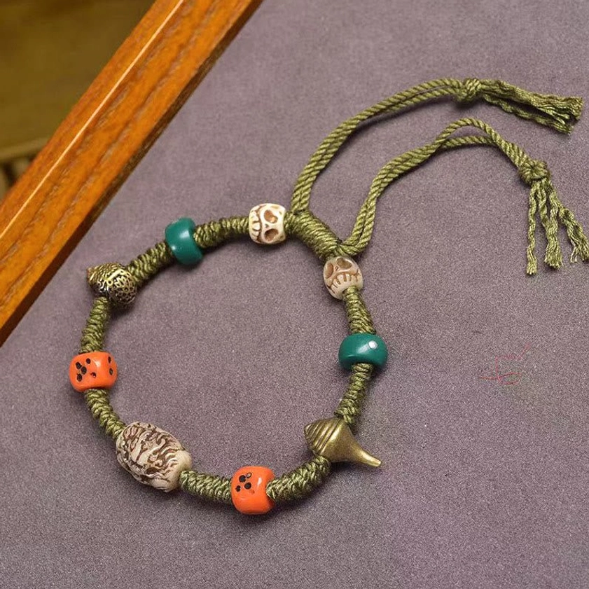 Handmade green rope Buddhist dragon bracelet with carved bead and adjustable tassel on wooden background
