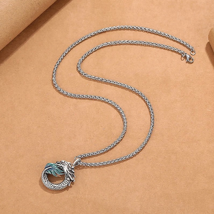 Dragon necklace flat lay featuring coiled wheat chain and miniature dragon pendant with enamel accents on kraft paper background