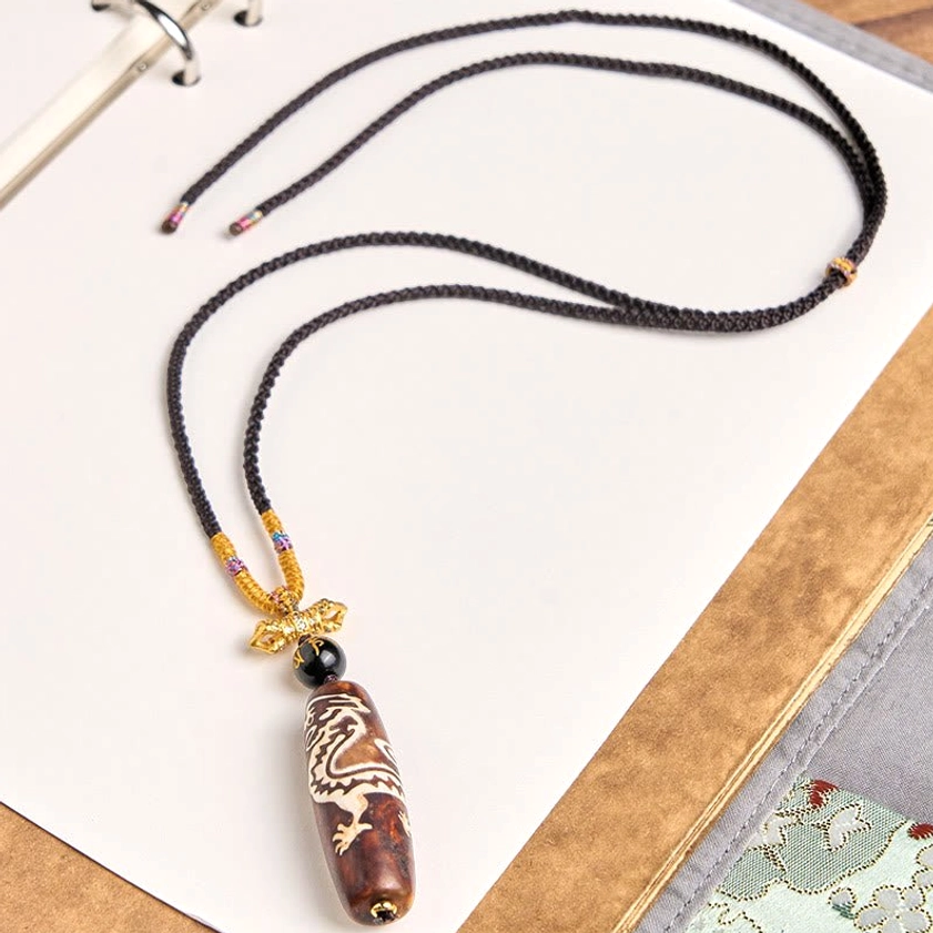 Buddhist dragon agate dzi bead necklace side angle view displaying braided cord texture and white dragon carving on natural stone
