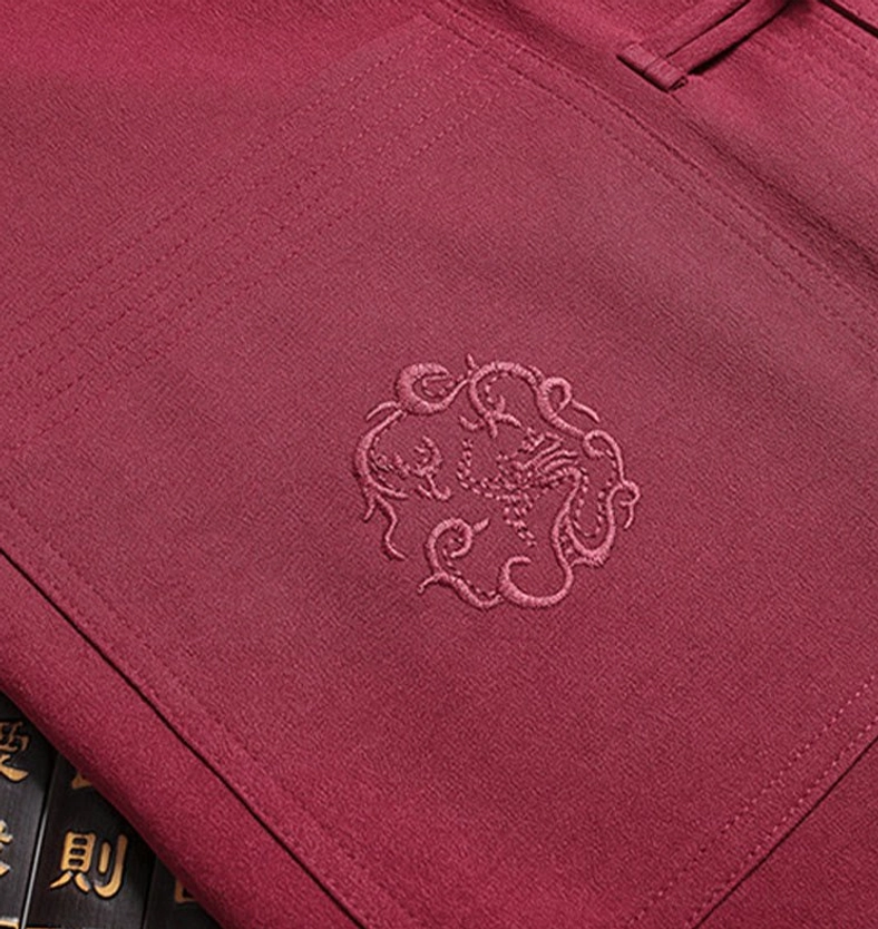 Tang suit dragon embroidery close-up - auspicious dragon pattern stitched on maroon fabric with embroidered patch pocket detail on vintage books background