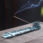 Dragon incense burner on woven placemat with burning incense and blue smoke, handcrafted alloy with patinated blue finish