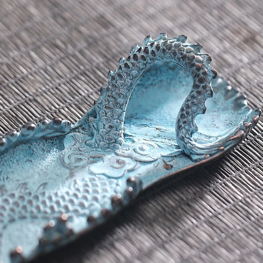 Close-up side view of hollow dragon body incense burner tray with patinated blue finish on wooden surface