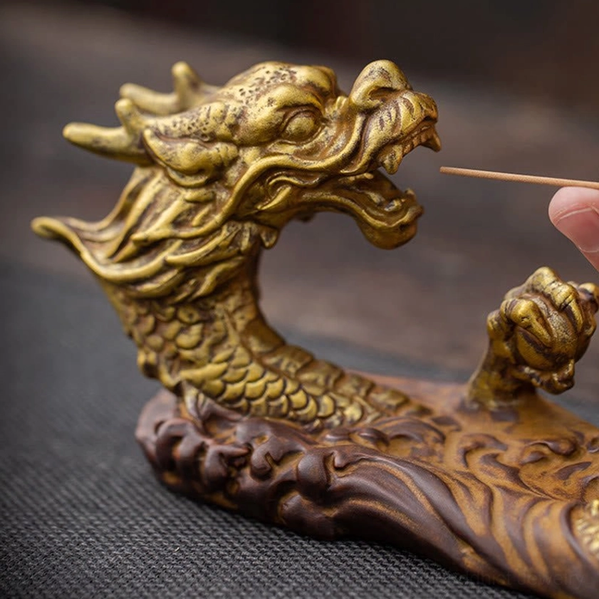 Close-up side view of golden dragon incense holder with hand placing incense stick in dragon's mouth